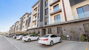 A modern apartment building with multiple floors, balconies, and a parking area with several cars. - Silkhaus Osus 7 (Riyadh)