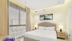 A modern hotel room with a large bed, two bedside tables with lamps, an air conditioning unit, and a window with blinds. - Silkhaus Osus 7 (Riyadh)