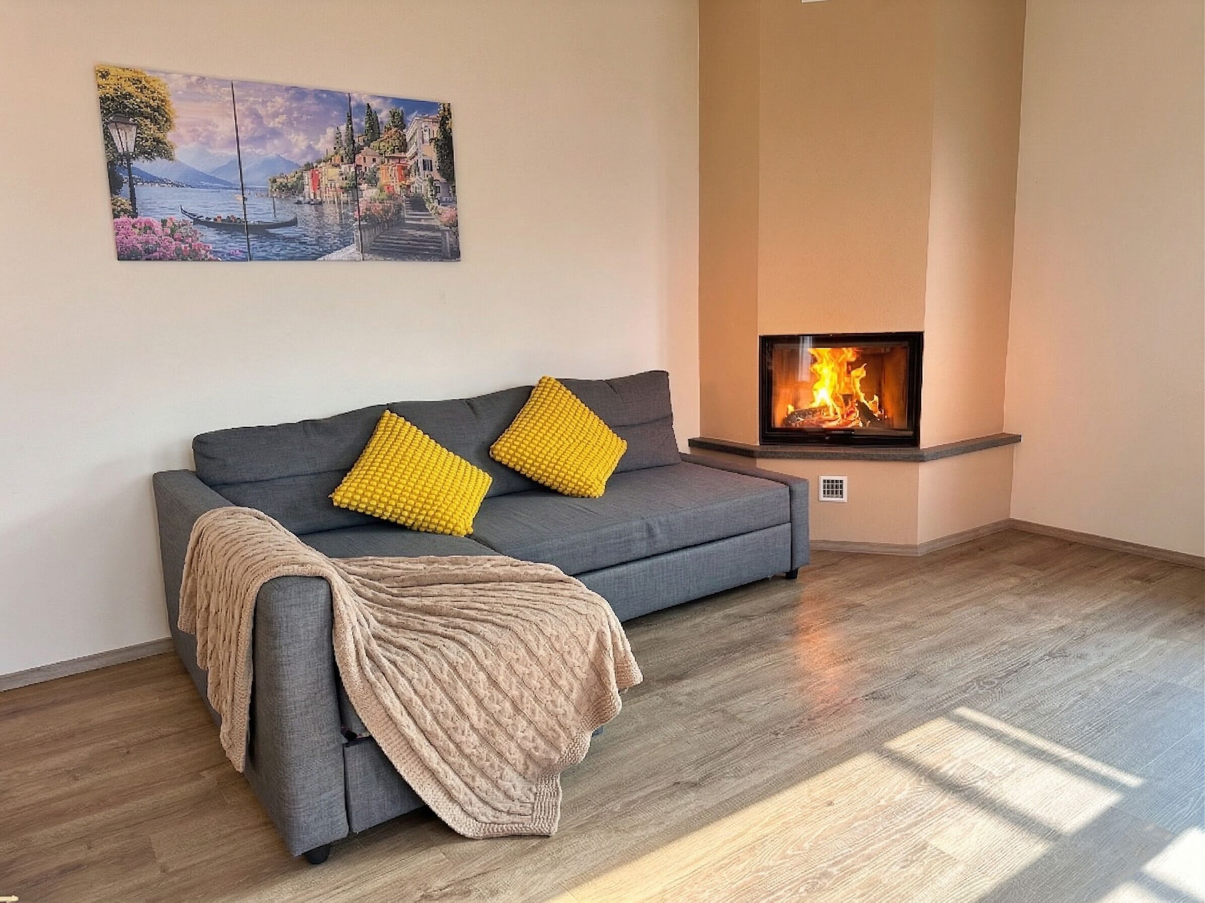 A living room with a grey sofa, yellow cushions, a beige throw blanket, a fireplace, and a painting on the wall.