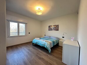 Un dormitorio con una cama, una mesita de noche, un escritorio, una ventana y un cuadro en la pared.
