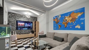 A modern living room with a checkered floor, a large flat-screen TV, a world map on the wall, and a fish tank. - Aphrodite's House Upon White Tower (Thessaloniki)
