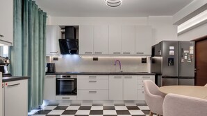A modern kitchen with white cabinets, a black and white checkered floor, a built-in oven, and a refrigerator with magnets. - Aphrodite's House Upon White Tower (Thessaloniki)