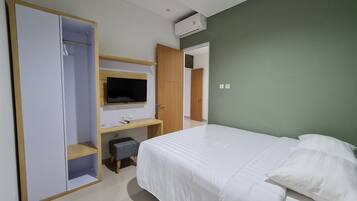 A bedroom with a bed, a TV mounted on a wooden shelf, a desk with a chair, and a wardrobe.