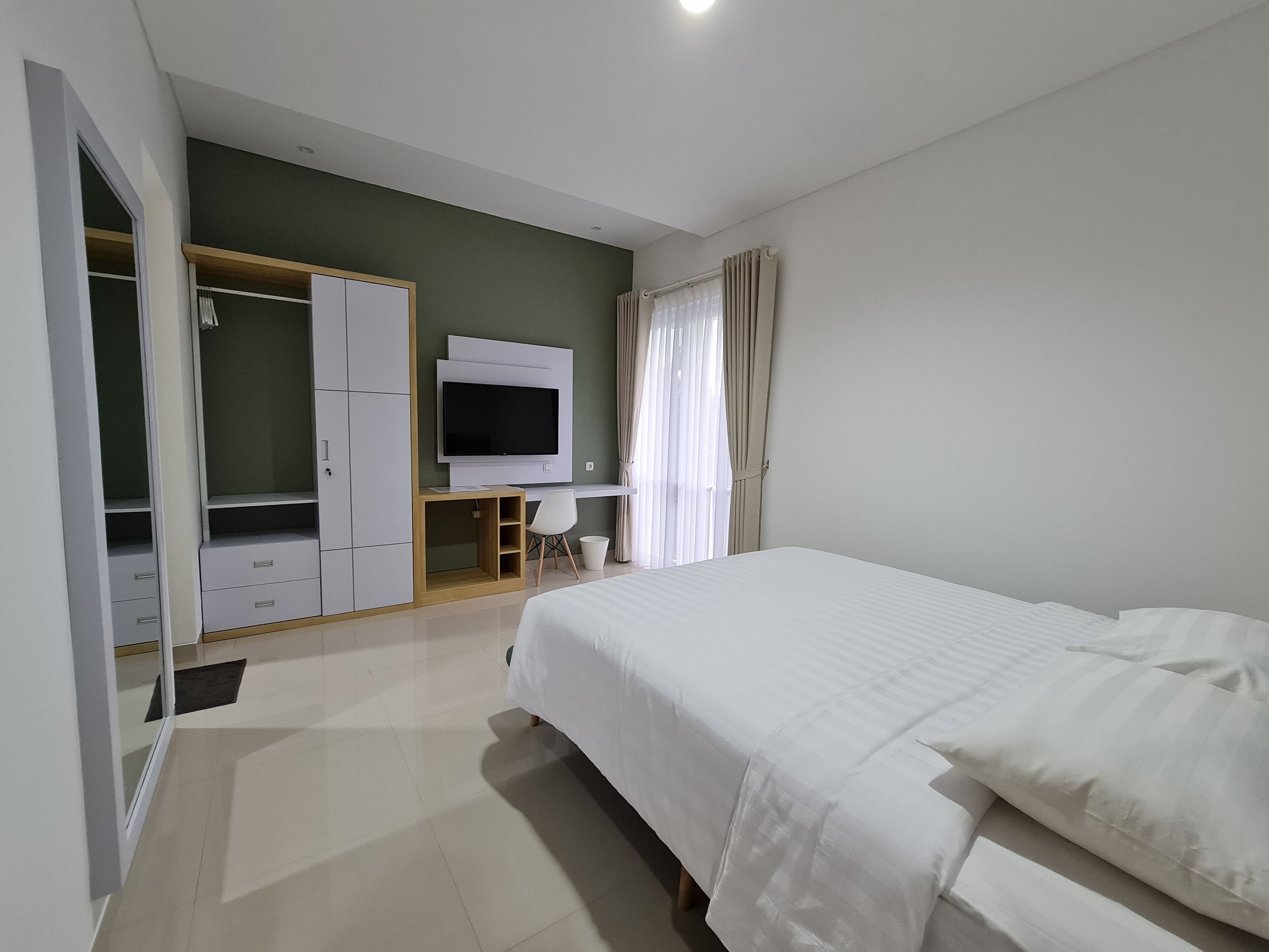 Un dormitorio con una cama, televisión montada en la pared, un escritorio y un armario.
