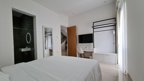 A modern hotel room with a large bed, a desk with a chair, a TV, and a bathroom with a mirror and sink. - Roemah Audy (Pogung Lor)