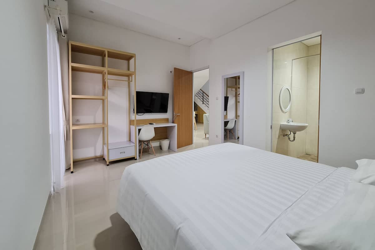 Un dormitorio moderno con cama, escritorio con silla, televisor, armario y baño con lavabo y espejo.