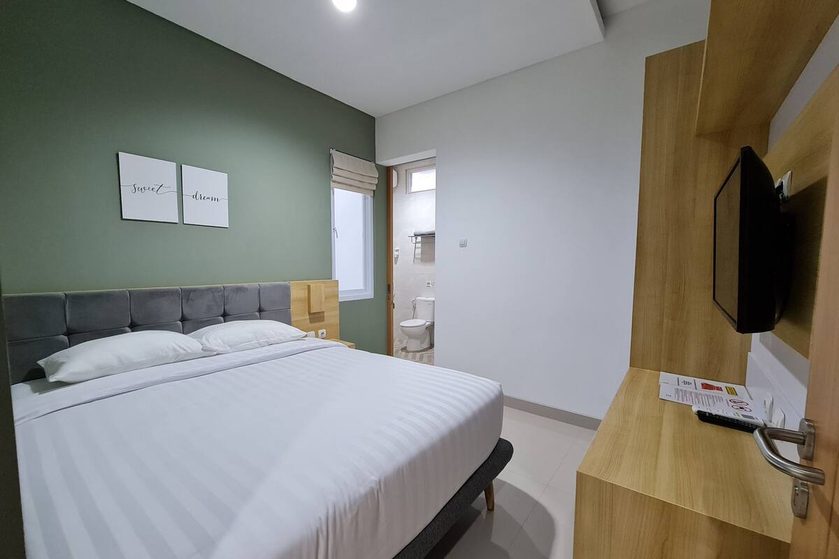 Una habitación de hotel con una cama, un escritorio de madera, un televisor y una ventana.
