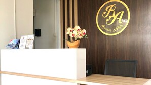 A reception desk with a wooden finish, a vase of flowers, and two circular logos with the initials "RA" and the name "Kroemer Andy". - Roemah Audy (Pogung Lor)