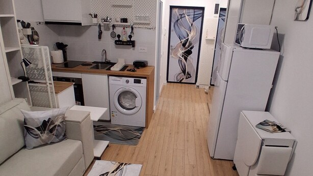 Eine kompakte Wohnung mit Küchenzeile, einer Waschmaschine, einem Essbereich und einem Wohnzimmer mit Sofa und Couchtisch.