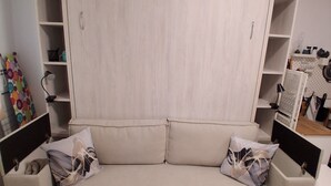 Ein beiges Sofa mit zwei Kissen, ein Holzschrank mit vielen Regalen und ein gemustertes Teppich auf dem Boden.