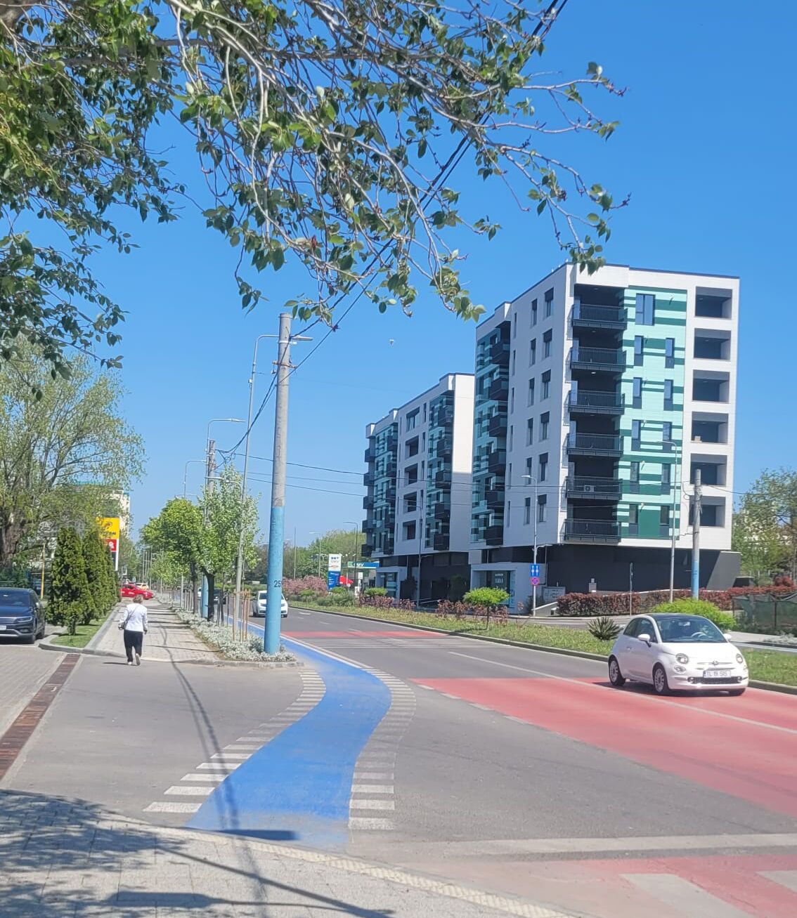 A modern multi-story building with balconies, a pedestrian walkway, and a road with a blue bike lane.