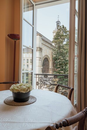 A room with a round table, a potted plant, and a view of a building with a tower through a window. - Le Marais Retreat, by Veeve (Paris)