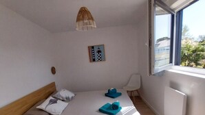 A bedroom with a bed, a bedside table, a lamp, a picture on the wall, and a window.