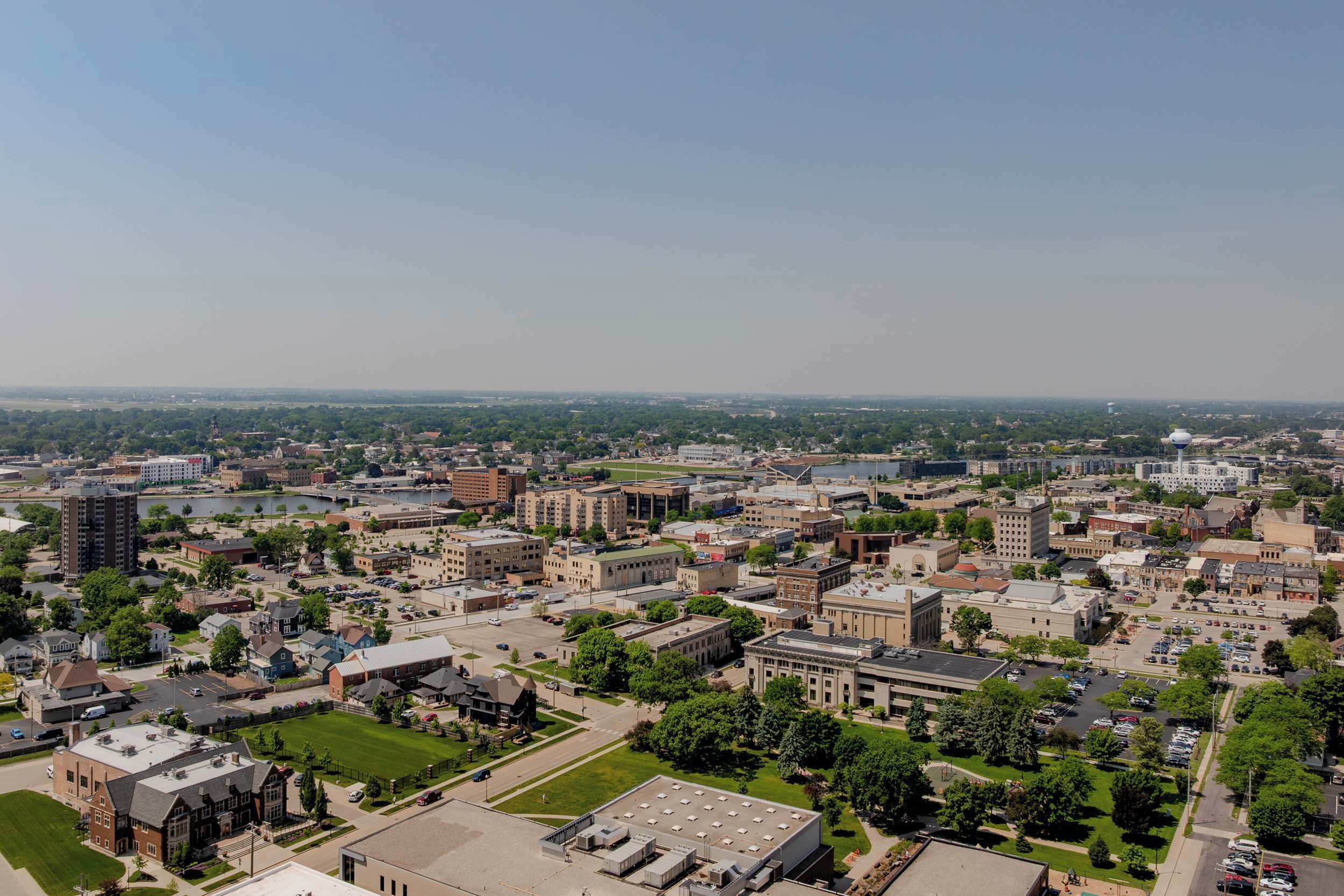 An aerial view of a university campus with multiple buildings, green spaces, and a large parking area.