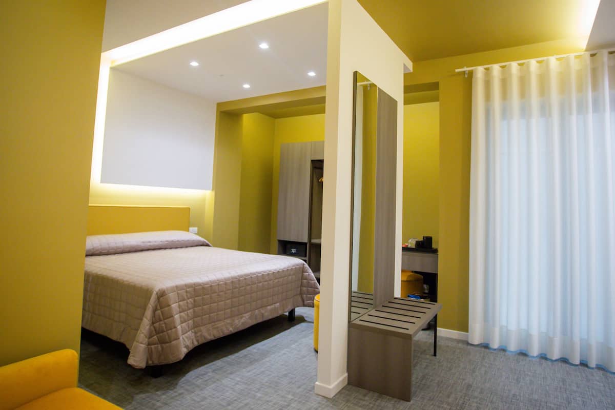 Ein Hotelzimmer mit Bett, einer Sitzbank, einem Spiegel und einem Kleiderschrank.