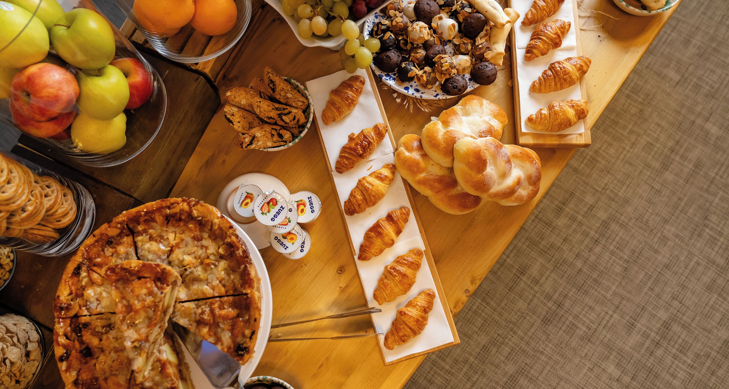 Un tavolo con diversi cibi, tra cui pizza, croissant e frutta.
