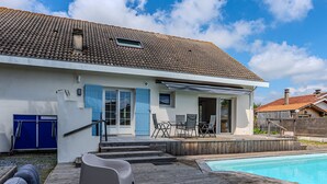 Een modern huis met een zwembad, een overdekt terras en een houten terras.