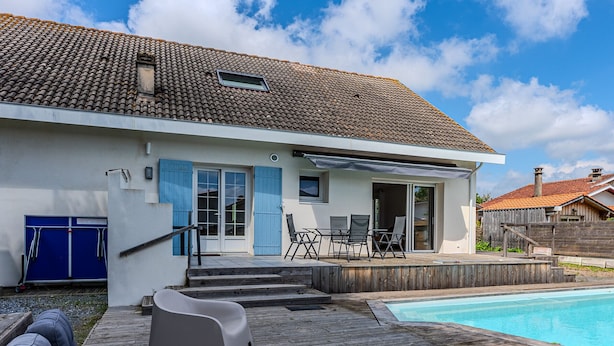 Ett modernt hus med en swimmingpool, en täckt uteplats och ett trädäck.