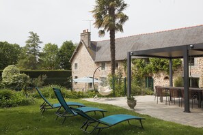 Une maison en pierre dotée d’un patio, d’un espace salon extérieur et d’un fauteuil suspendu.