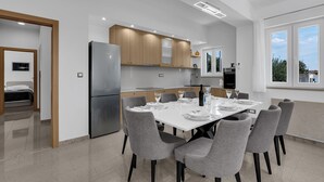 Une cuisine moderne avec un coin repas, comprenant un grand îlot central, des placards intégrés et une vue sur l’extérieur.