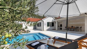 Een zwembadgedeelte met ligbedden, een tafel en een witte parasol.