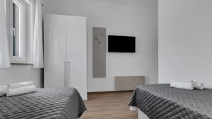 Een moderne hotelkamer met twee bedden, een kledingkast, een flatscreen-televisie en een raam met gordijnen.