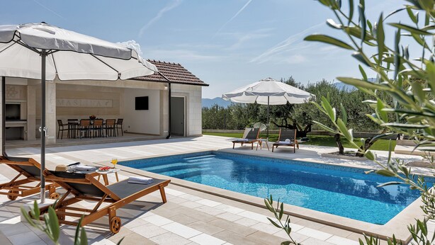 Une piscine avec des chaises longues et des parasols, un espace bar et une vue sur les montagnes.