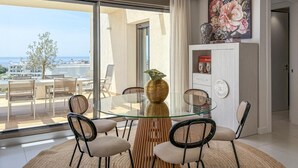 Un espace de repas moderne avec une table et des chaises en verre, un vase décoratif et une vue sur la ville grâce à de grandes fenêtres.