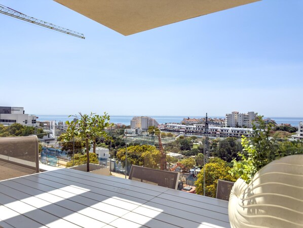 A terrace with a view of the sea and cityscape, including buildings and construction cranes.