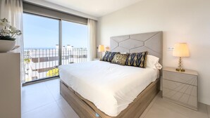 Une chambre d’hôtel moderne avec un grand lit, une table de chevet avec une lampe et une vue sur la ville depuis un balcon.