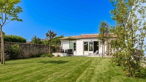 A house with a stone wall, a grassy lawn, and a patio with outdoor furniture. - Holiday home with lush garden in Loix (Loix)