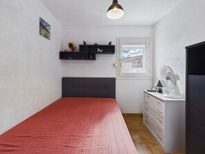 A bedroom with a bed, a dresser, a shelf with items, a window, and a fan.