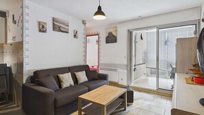A living room with a sofa, a wooden coffee table, a ceiling light, a sliding glass door, and a fan. - 2-room apartment with loggia in Marseillan-Plage (Marseillan-Plage)
