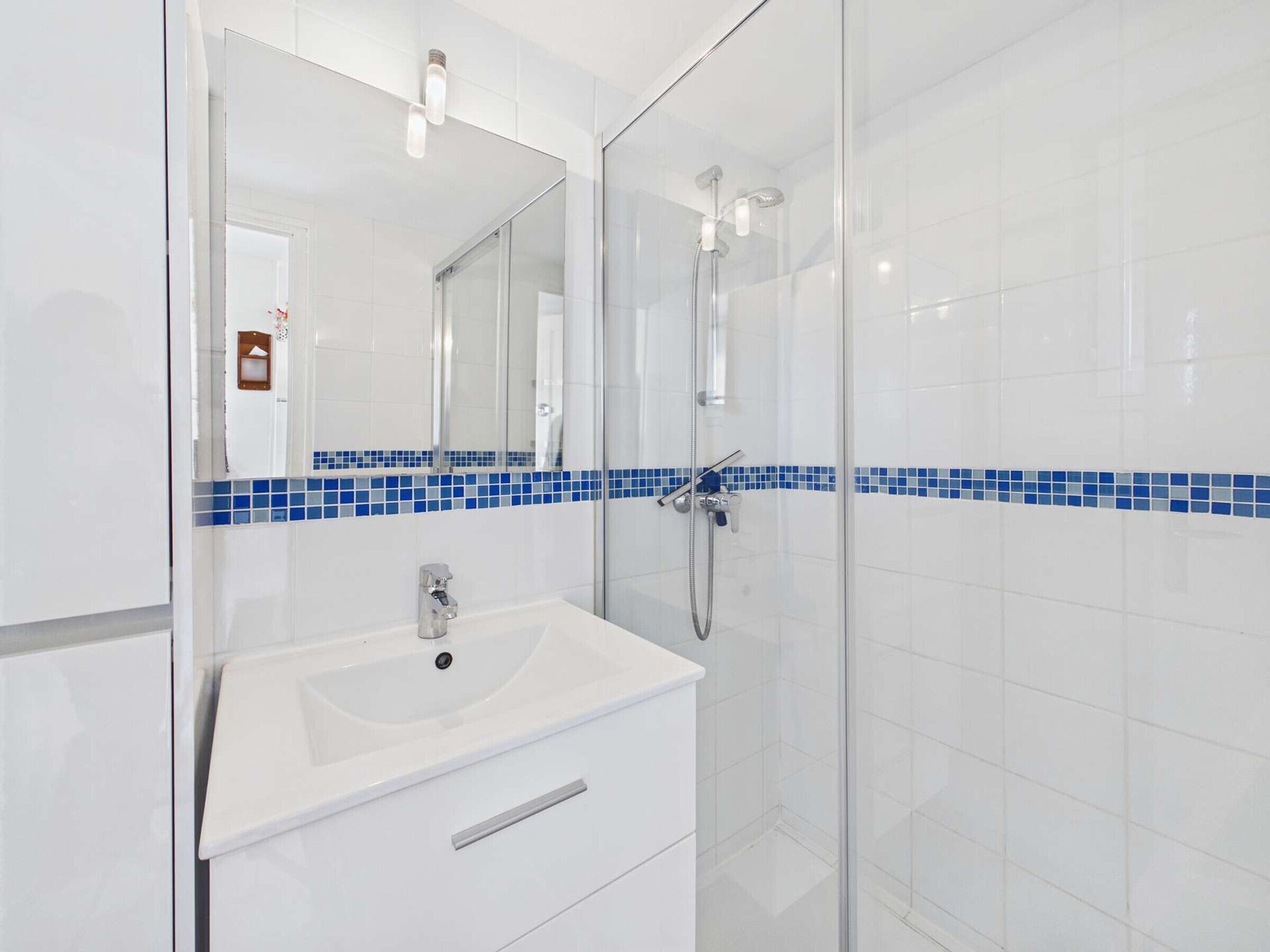 A modern bathroom with a glass shower enclosure, a white sink, and a mirror with a blue-tiled backsplash.