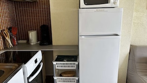 Une cuisine compacte équipée d’un four à micro-ondes, d’un réfrigérateur et d’un évier. On y trouve également des paniers et des ustensiles de cuisine sur le plan de travail.