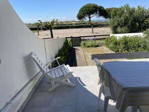 Un patio con mesa y sillas, un muro blanco y vistas a la playa y árboles.