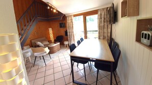 A dining area with a long table and chairs, a staircase, a sofa, and a lamp.
