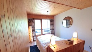 A wooden-paneled bedroom with a bed, bedside lamps, a mirror, and a view of the outdoors through a door.