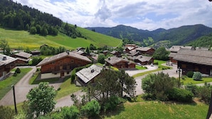 A village with traditional wooden houses, surrounded by green hills and mountains.