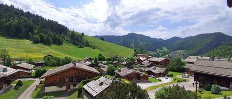 A village with traditional wooden houses, surrounded by green hills and mountains.
