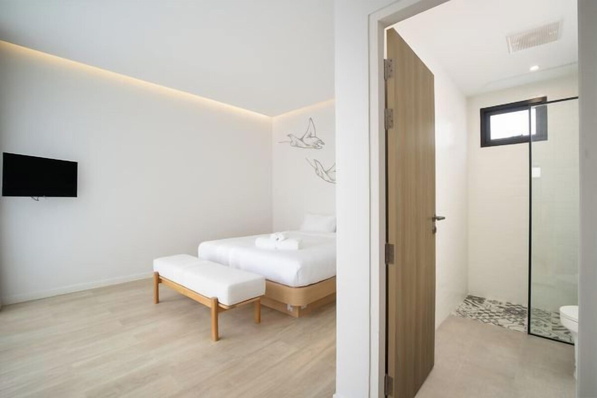 A modern bedroom with a bed, a bench, and a TV mounted on the wall.