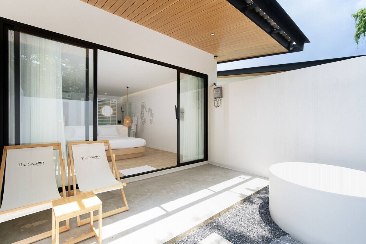 A modern hotel room with a large sliding glass door leading to a balcony, a minimalist bathroom, and a small seating area with a table and chairs.