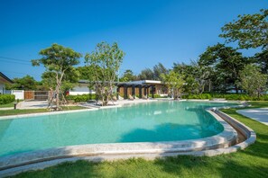 Une piscine à bord incurvé, entourée de pelouse et d’arbres.