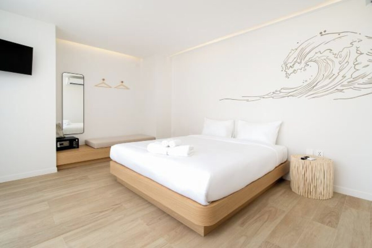 Un dormitorio moderno con estructura de cama de madera, ropa de cama blanca, televisor montado en la pared y una mesita de noche pequeña.