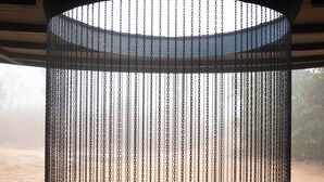 Une fontaine circulaire, délimitée par une chaîne, entourée d’un sol carrelé et offrant une vue sur un paysage naturel.