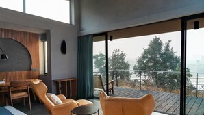 Un salon moderne avec une terrasse en bois, un coin repas et une vue sur les arbres et l’eau.