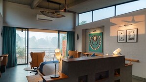 Une chambre d’hôtel moderne dotée d’une grande porte-fenêtre coulissante donnant sur un balcon, d’un bureau avec une lampe et d’une œuvre d’art fixée au mur.