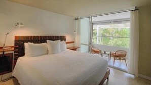 A hotel room with a large bed, a nightstand, a lamp, a window with curtains, and a view of greenery outside. - Private Island Suite w/ Terrace & Balcony @Islamorada - Coconut Palm Suite (Islamorada)