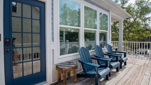A wooden deck with blue Adirondack chairs and a small wooden table. - Sea Y'all: Early Bird Special! (Oak Island)