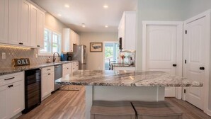 A modern kitchen with white cabinets, a marble countertop, and a central island with bar stools. - Sea Y'all: Early Bird Special! (Oak Island)